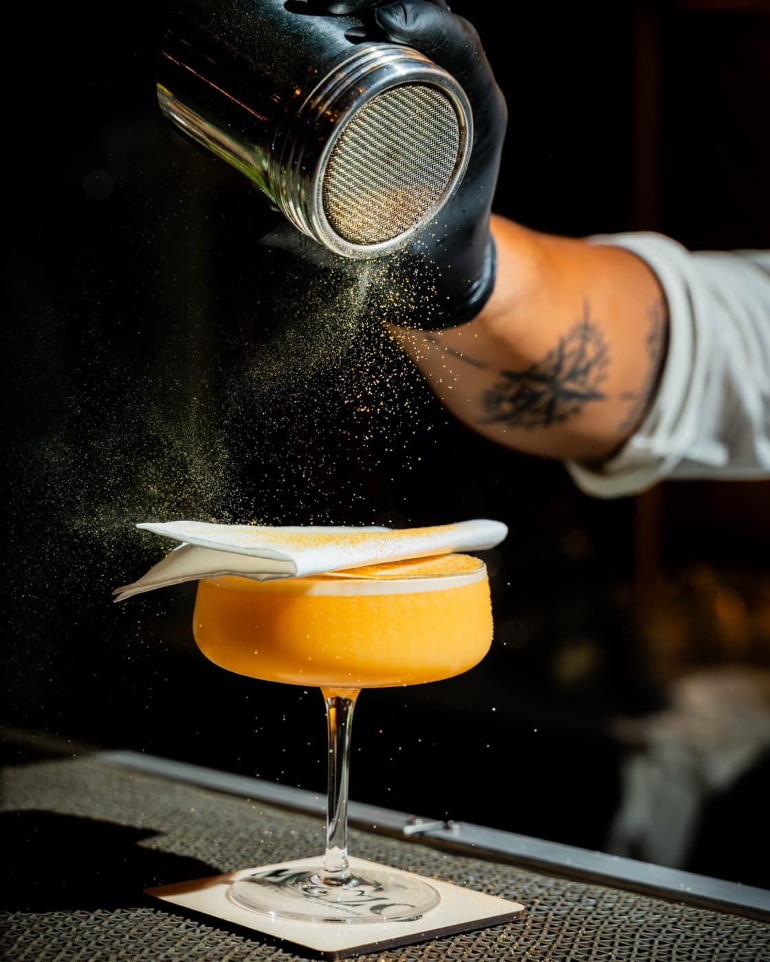 Bartender misting an amber sour in a coupe