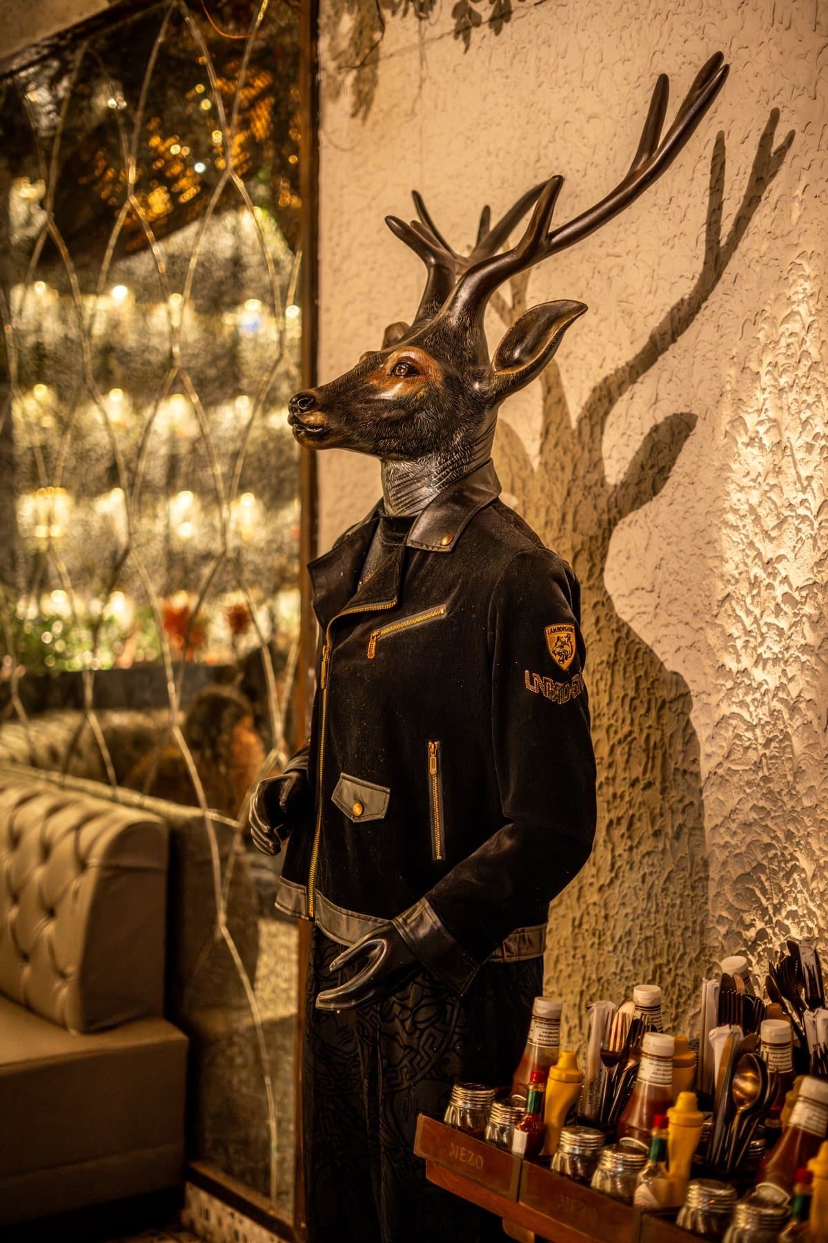 Deer butler sculpture in uniform beside the glowing bottle wall